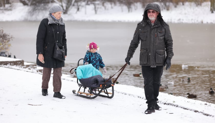 Na zdjęciu: mężczyzna ciągnący sanki po śniegu, nad wrocławską fosą miejską. Obok sanek idą kobieta oraz mała dziewczynka.
