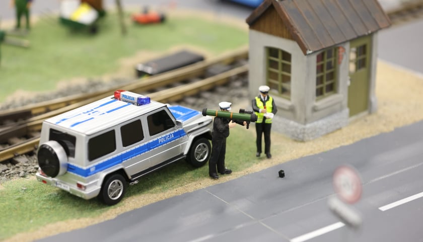 Na zdjęciu scenka z Kolejkowa: radiowóz i policjant z granatnikiem zamiast radaru
