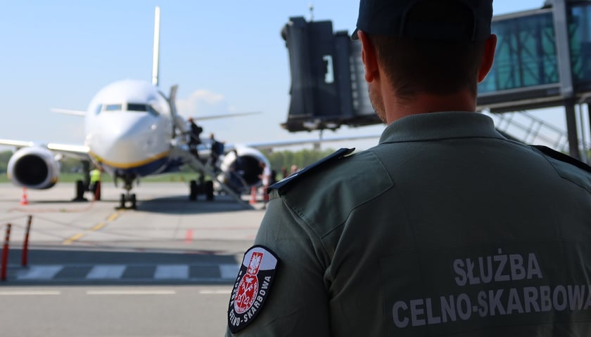 Funkcjonariusz służby celno-skarbowej w mundurze, w tle samolot