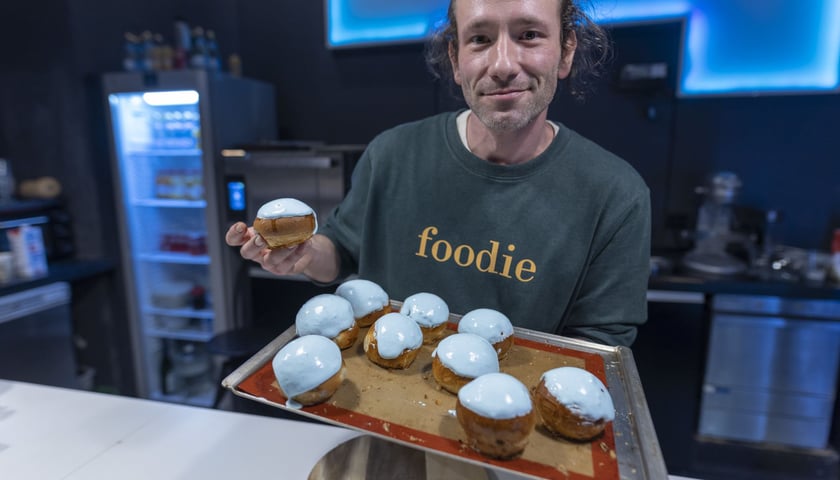 Na zdjęciu: kucharz Mateusz Zielonka trzymający tacę z pączkami oblanymi jasnobłękitnym lukrem