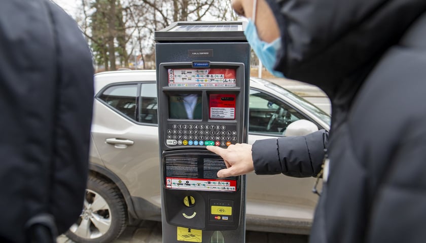 Na zdjęciu: mężczyzna obsługujący automat do parkowania, samochód na dalszym planie