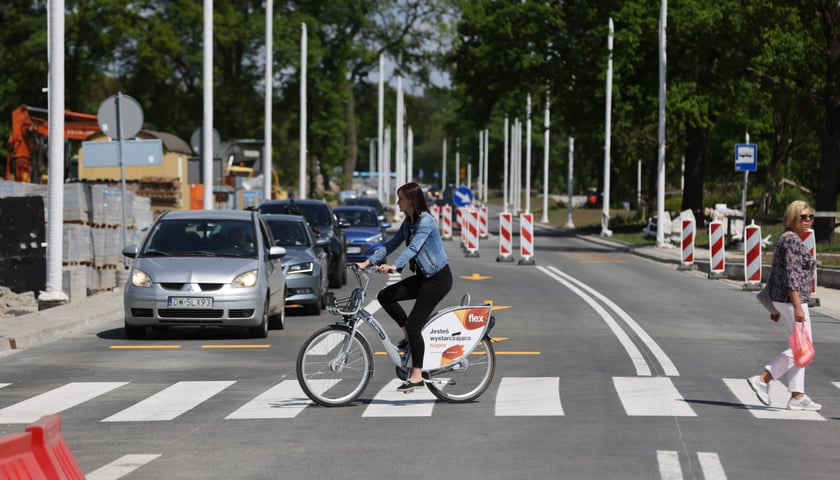 Rowerzystka przejeżdżająca przez pasy i stojące samochody na otwartym odcinku AWW