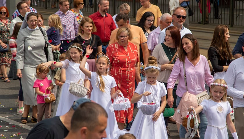 Procesja Bożego Ciała 2022 we Wrocławiu. Wierni idą ulicą, dziewczynki w białych sukienkach sypią płatkami kwiatów