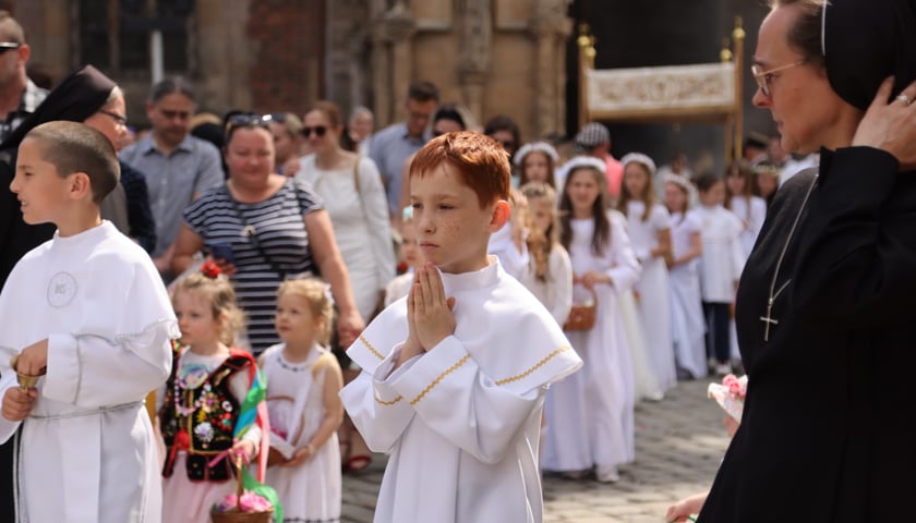 Procesja Bożego Ciała we Wrocławiu 2023. Na pierwszym planie chłopiec w białej albie ze złożonymi rękami