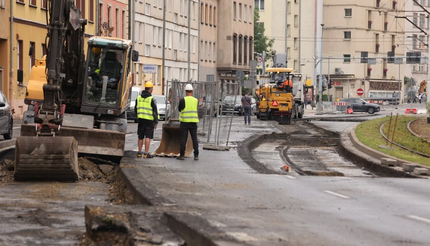 Rozkopana jezdnia, koparka i dwójka robotników w żółtych kamizelkach; ulica Kazimierza Wielkiego