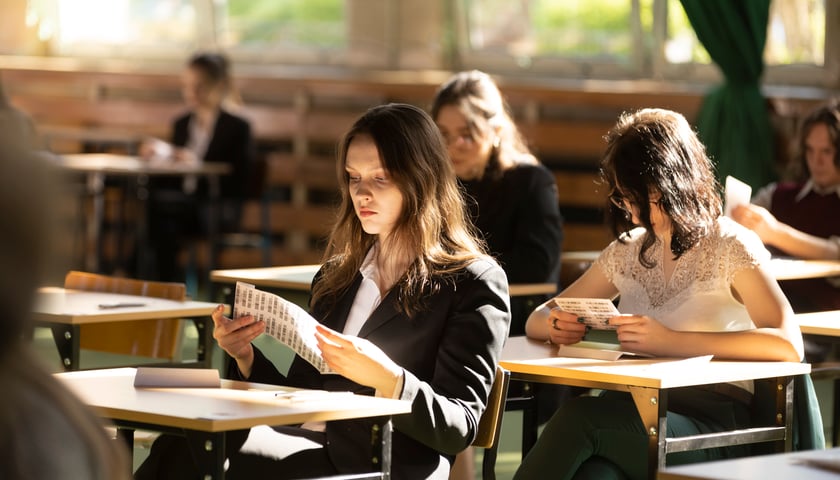Uczniowie VII LO we Wrocławiu siedzą w ławkach podczas matury 2023 z języka polskiego. Na pierwszym planie dwie uczennice czytają arkusze.