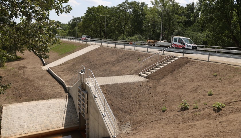 Wał i ulica Ślęzoujście, na niej samochody wykonawcy, w dole potok Ługowina