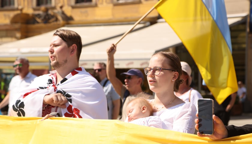Mężczyzna i kobieta z małym dzieckiem na ręku. W tle widać ukraińską flagę