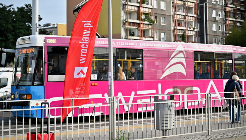 Tramwaj linii 13 jedzie na nowodworską pętlę. Na pierwszym planie chorągiewka wroclaw.pl sygnalizująca, że tu znajduje się punkt informacyjny o zmianach w komunikacji miejskiej.  