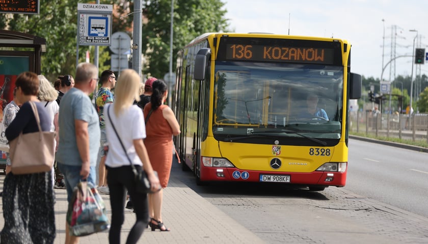 Zdjęcie ilustracyjne przedstawiające ludzi na przystanku autobusowym.