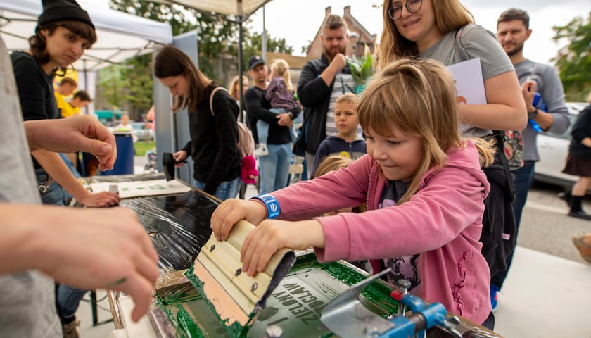 Dziewczynka wykonuje napis w technologii sitodruku podczas Zielonego Pikniku w 2021 r.