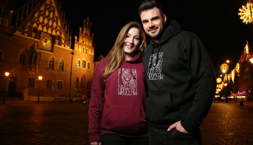Na zdjęciu para stojąca na wrocławskich rynku ubrana w bluzy z herbem Wrocławia.