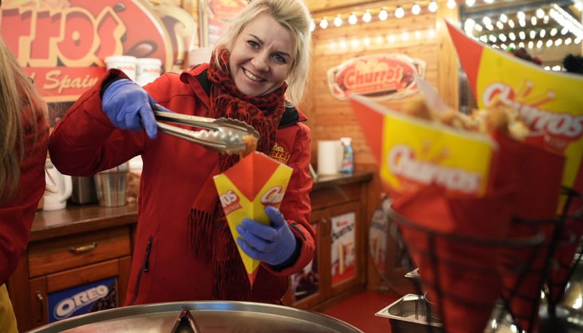 Kobieta w czerwonym płaszczu nakłada churros przy jednym ze stoisk Jarmarku Bożonarodzeniowego
