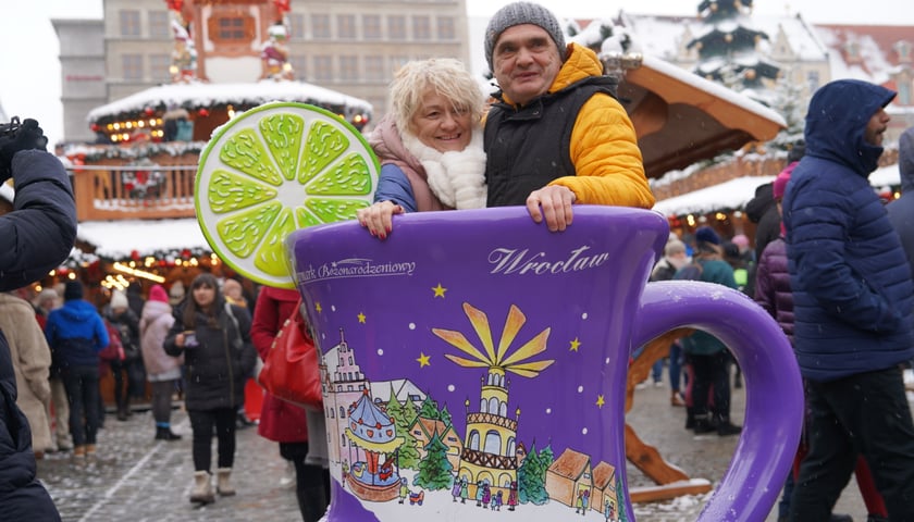Jarmark Bożonarodzeniowy we Wrocławiu. Kobieta i mężczyzna pozują do zdjęcia w wielkim kubeczku buciku
