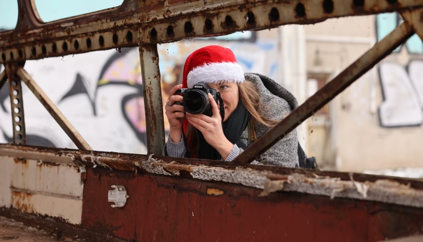 Kobieta z aparatem fotograficznym i w czapce Mikołaja oparta o burtę starego autobusu. Mikołajki w Zajezdni Popowice, Wrocław 9 grudnia 2023.