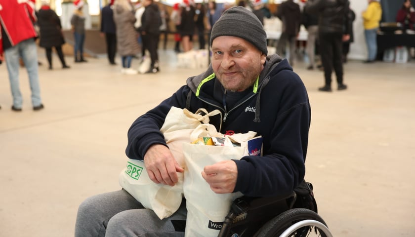 Mężczyzna na wózku inwalidzkim trzymający na kolanach dwie torby ze świątecznymi paczkami