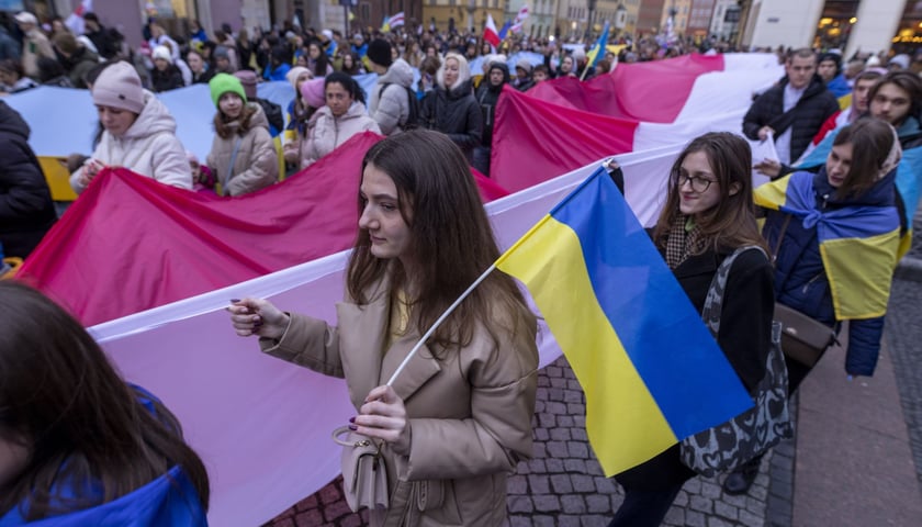 Tłum niesie flagę Polski. Na pierwszym planie młoda kobieta z flagą Ukrainy. Uroczystości we wrocławskim Rynku 24 lutego 2023 w rok po wybuchu wojny. 
