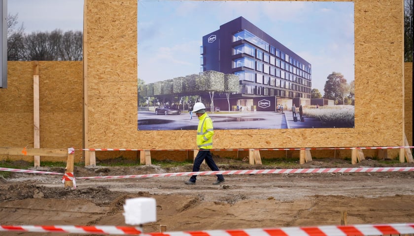 Budowlaniec w białym kasku spacerujący na tle wizualizacji hotelu