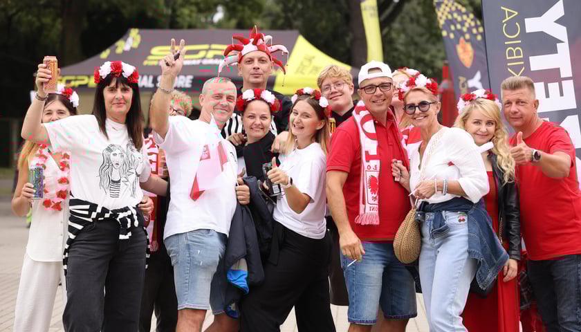 Żużel na Olimpijskim. Na zdjęciu kibice - kobiety i mężczyźni, mają czapki, wianki i szaliki w biało- czerwonych barwach