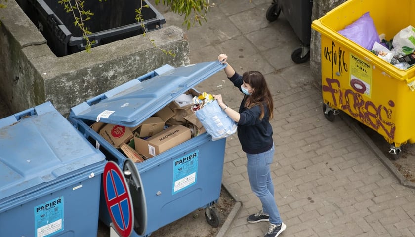 Жінка викидає сміття у вуличні контейнери.