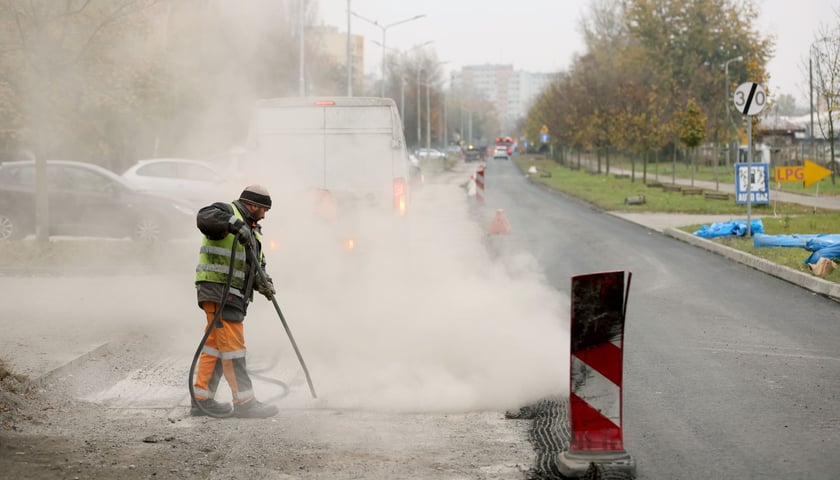 Osoba w roboczym stroju z dymiącym urządzeniem na remontowanej ulicy Balonowej