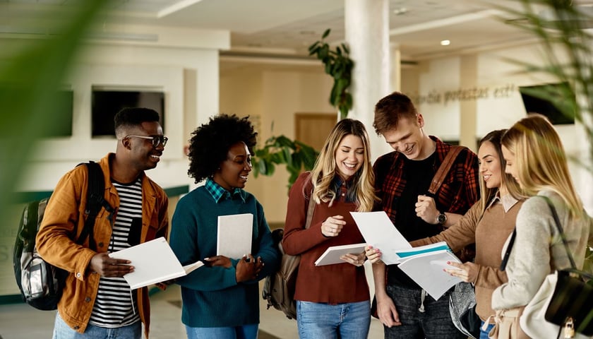 W korytarzu stoi grupa uśmiechniętych studentek i studentów.