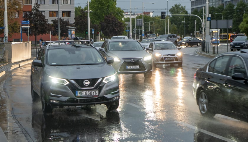 Samochód z włączonymi światłami jedzie w deszczu po rondzie Reagana