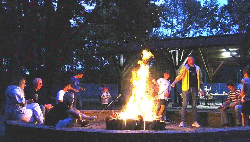 Nocowanka w Parku Glinianki. Na zdjęciu kilka osób stoi wokół ogniska