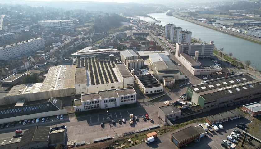 Na zdjęciu widoczne z góry budynki, ulica, pojazdy i rzeka./ The photo shows buildings, a street, vehicles and a river visible from above.