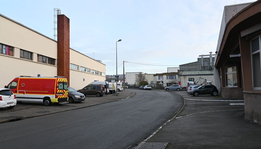 Na zdjęciu widoczna ulica wraz z budynkami po obu stronach i stojące samochody pod budynkami./ The photo shows a street with buildings on both sides and cars parked in front of the buildings.