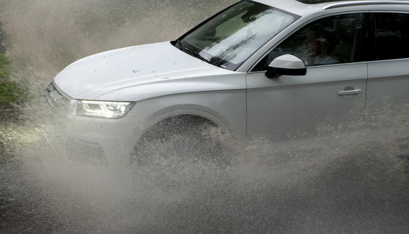 Samochód jedzie przez mocno zalaną drogę - zdjęcie ilustracyjne.