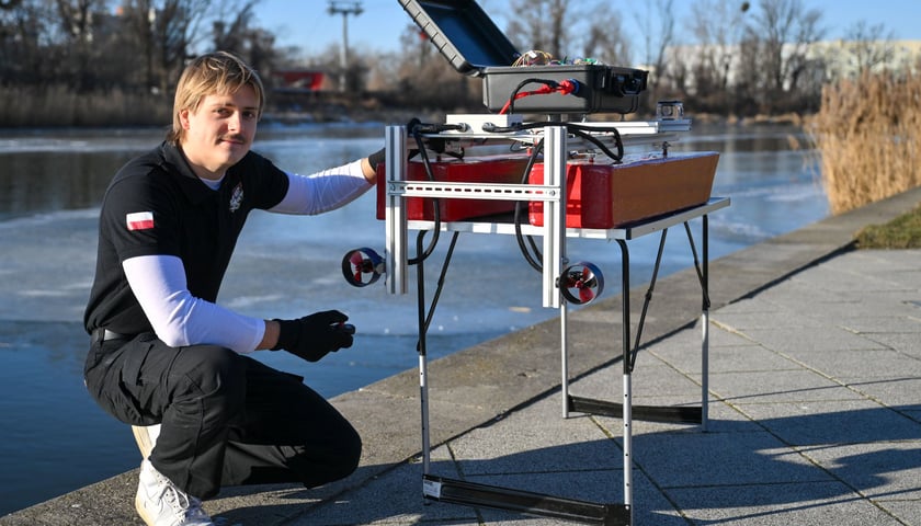 Młody naukowiec kucający obok drona wodnego F.O.K.A.