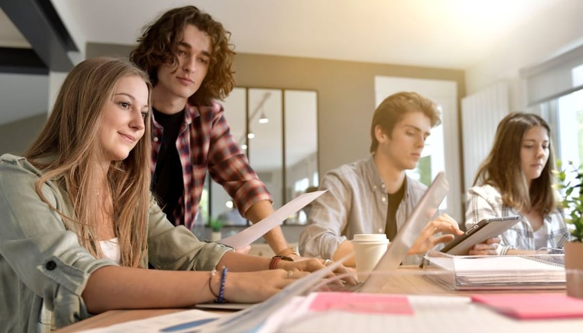 Studentki i studenci przy stole, na którym znajdują się notatki i pomoce naukowe