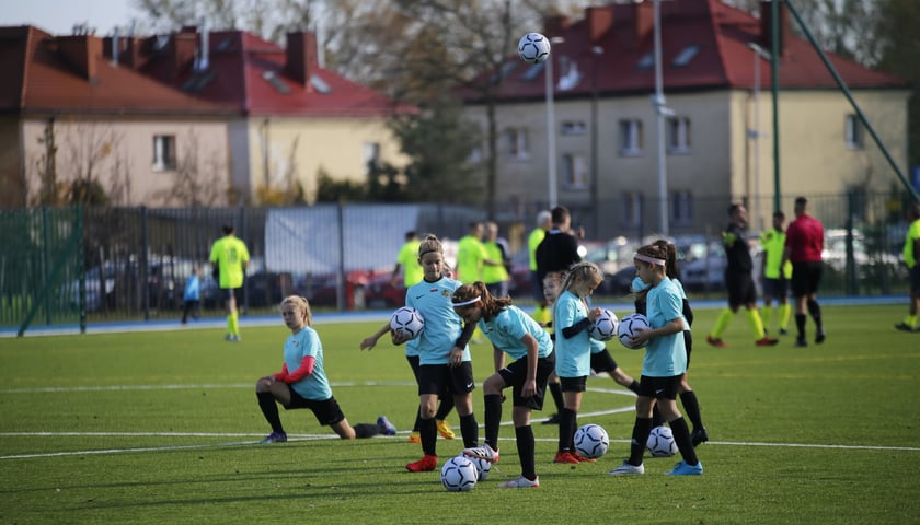 Powiększ obraz: Na zdjęciu grupa dziewcząt na boisku z piłkami podczas rozgrzewki na stadionie przy ul. Asnyka w Katowicach