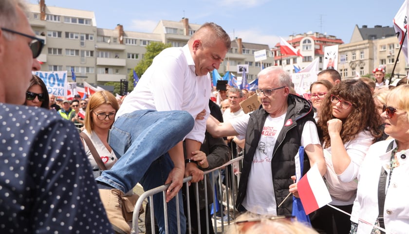 Powiększ obraz: Wiec Donalda Tuska we Wrocławiu. Bartosz Arłukowicz rusza z pomocą do osoby, która źle się poczuła i przeskakuje przez płot