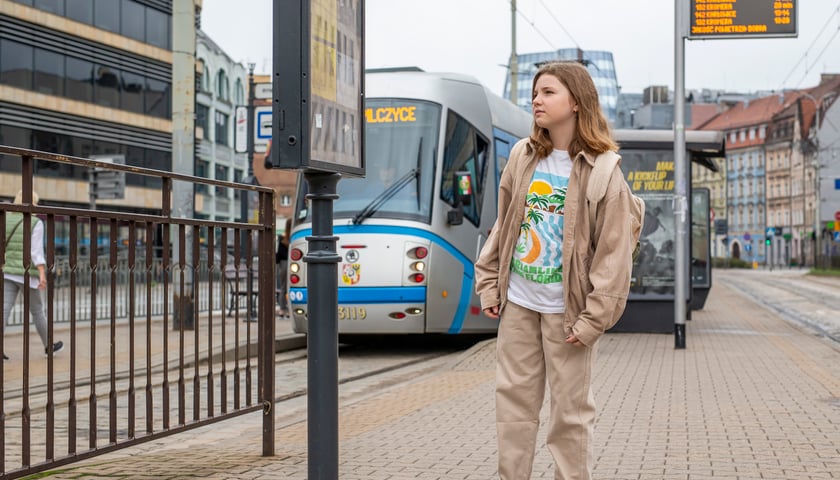 Powiększ obraz: Dziewczynka z plecakiem sprawdza rozkład jazdy na przystanku tramwajowym