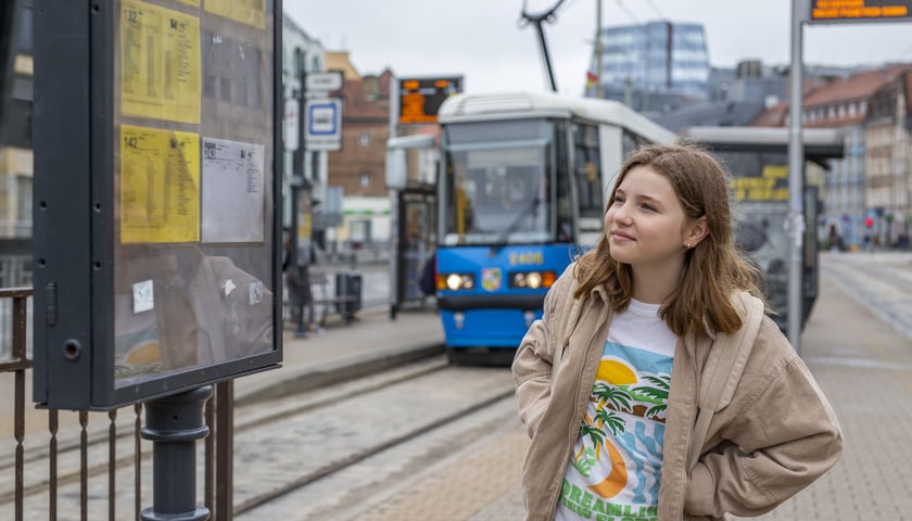 Powiększ obraz: Dziewczynka sprawdzająca rozkład jazdy na przystanku