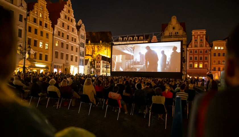 Widzowie podczas seansu Festiwalu Nowe Horyzonty w Rynku. Widać telebim oraz wyświetlany na nim film, w tle kamienice