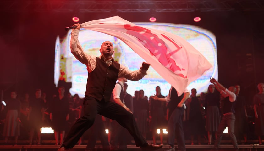 Spektakl "75, czyli powojenna historia Wrocławia". Mężczyzna na scenie z białą flagą z napisem "Solidarność"