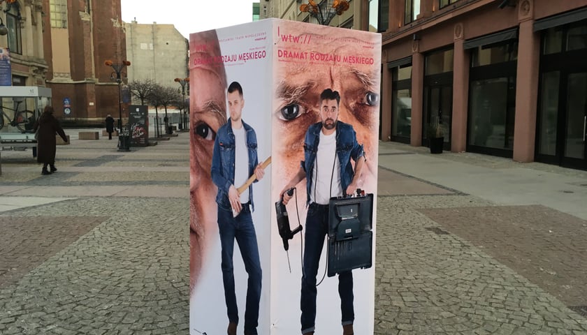 Reklama stojąca na Świdnickiej z mężczyznami trzymającymi w dłoniach siekierę i wiertarkę