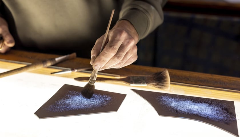 Męskie dłonie malujące pędzlem po kawałku szkła (zdjęcie ilustracyjne)