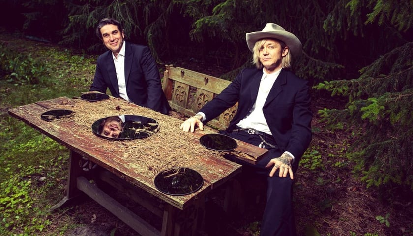 Na zdjęciu Marcin Dorociński i Wojtek Mazolewski siedzą przy drewnianym stole na polanie