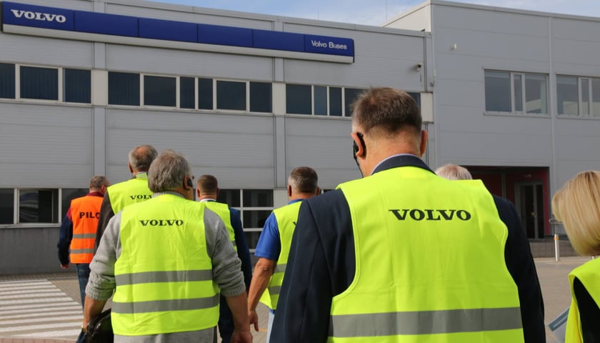 Pracownicy w żółtych kamizelkach idący w kierunku fabryki Volvo Buses