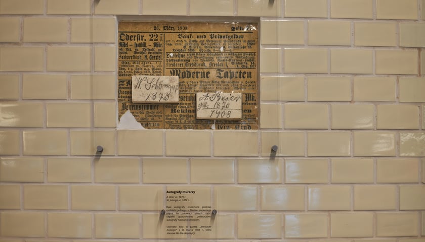 Powiększ obraz: Na zdjęciu za szybą dwie cegły z autografami murarzy, którzy budowali piekarnię; cegły umieszczono na tle zdjęcia gazety z 1908 r., w którą były owinięte