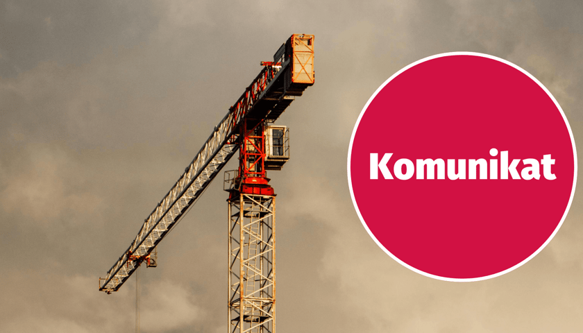 W tle dźwig na tle chmur, w kółku napis: Komunikat