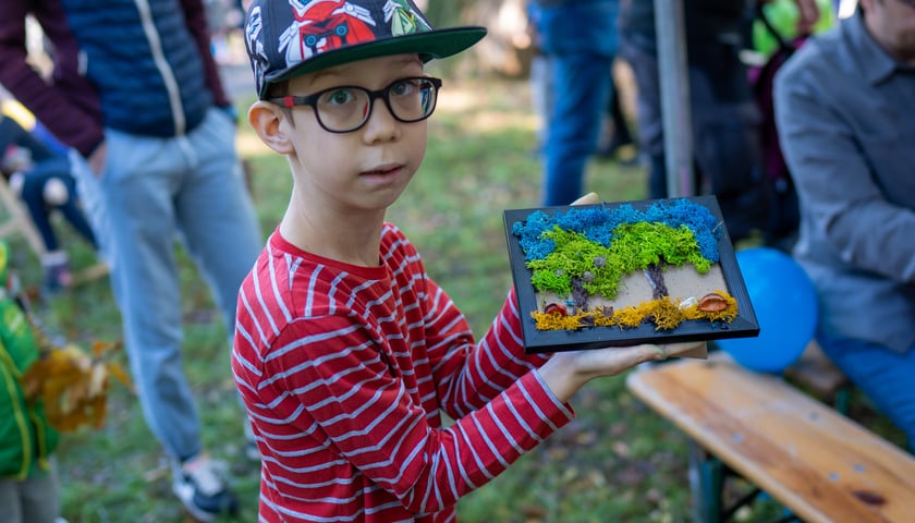 Chłopiec w kolorowej czapce bejsbolówce trzyma obrazek z drzewami