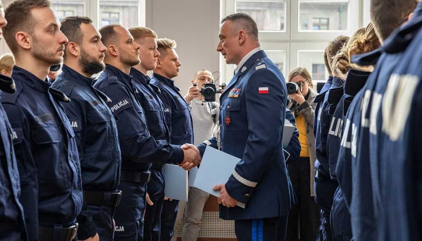 Ślubowanie nowych policjantów. Na zdjęciu mężczyzna w policyjnym mundurze gratuluje młodym policjantom stojącym w szeregu