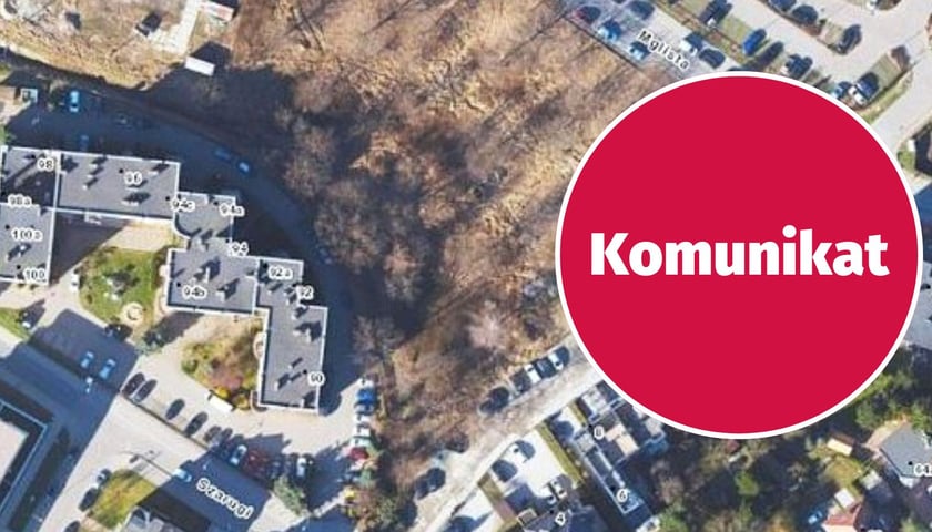 Widok z lotu ptaka na fragment osiedla z budynkami, ulicami i terenem zielonym, w prawym części czerwony okrąg z białym napisem "komunikat"
