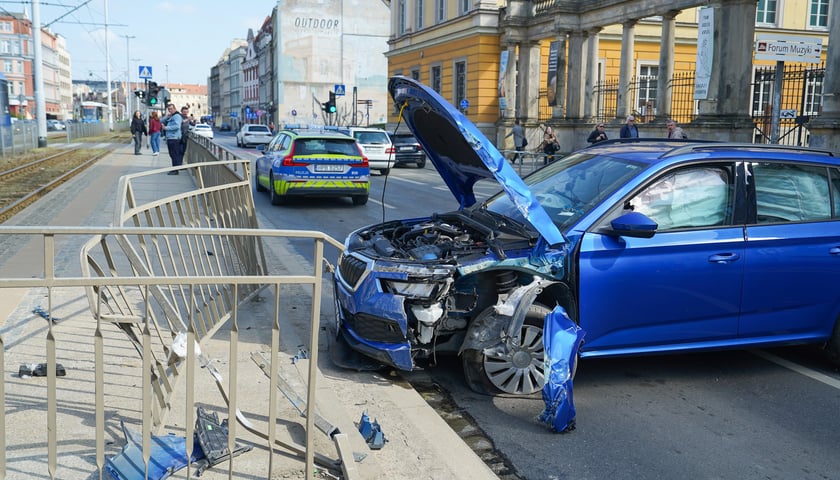 Rozbite auto stoi w poprzek ulicy Kazimierza Wielkiego przy uszkodzonych barierkach oddzielających przystanek tramwajowy.