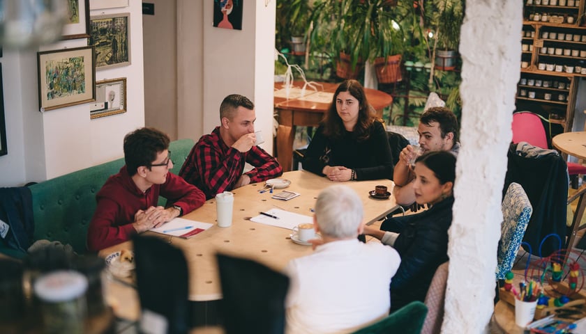 <p>Grupka os&oacute;b siedzących przy stole podczas warsztat&oacute;w, zdjęcie archiwalne.</p>